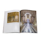 Open book showing a grand hallway with decorative ceiling and marble floor.