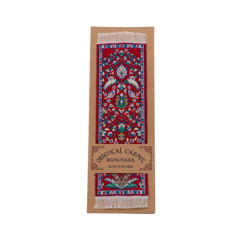 Oriental carpet bookmark with red decorative design on a cardboard backing.