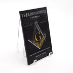 Book titled 'Freemasonry Defined' with a Square and Compass on a stand against a white background