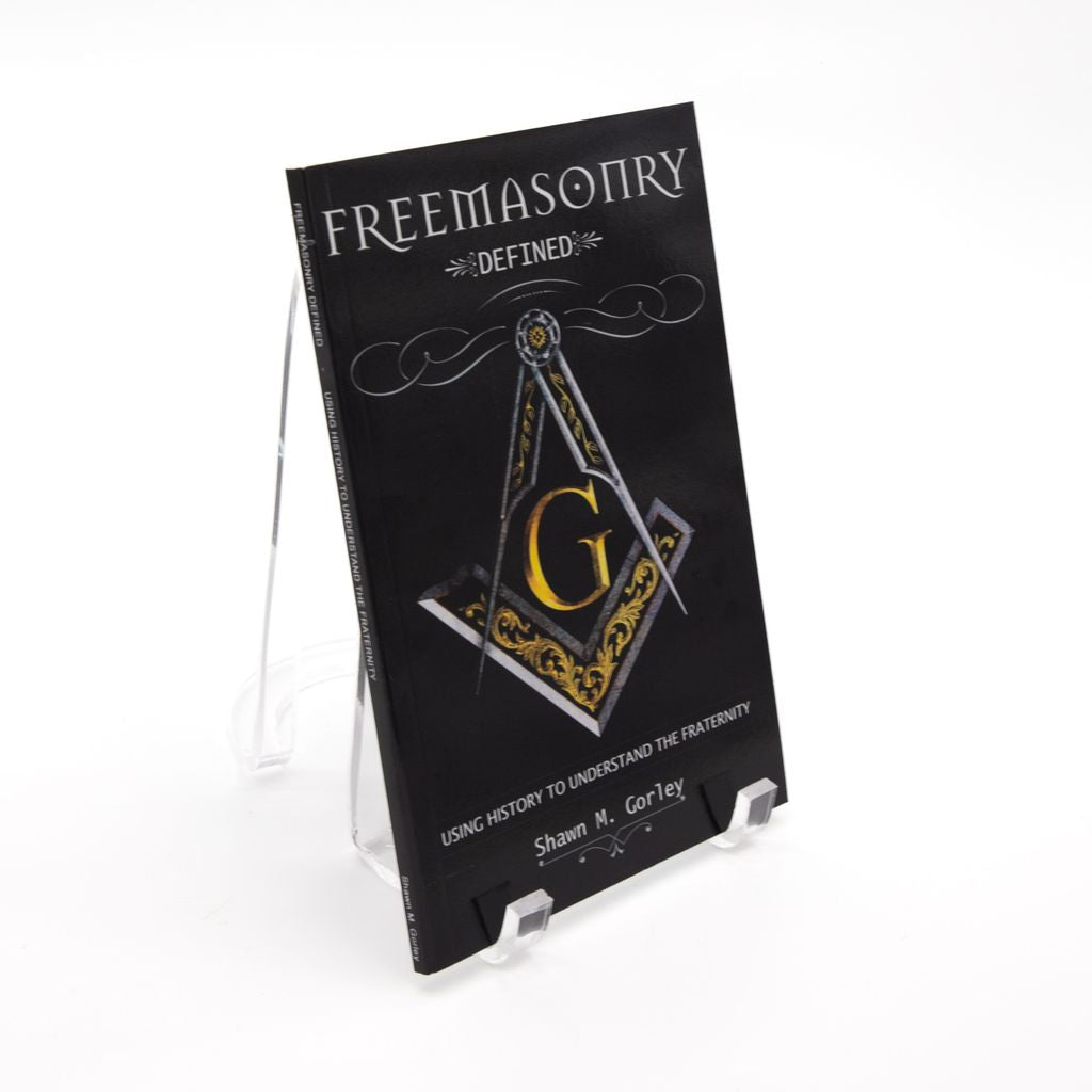 Book titled 'Freemasonry Defined' with a Square and Compass on a stand against a white background