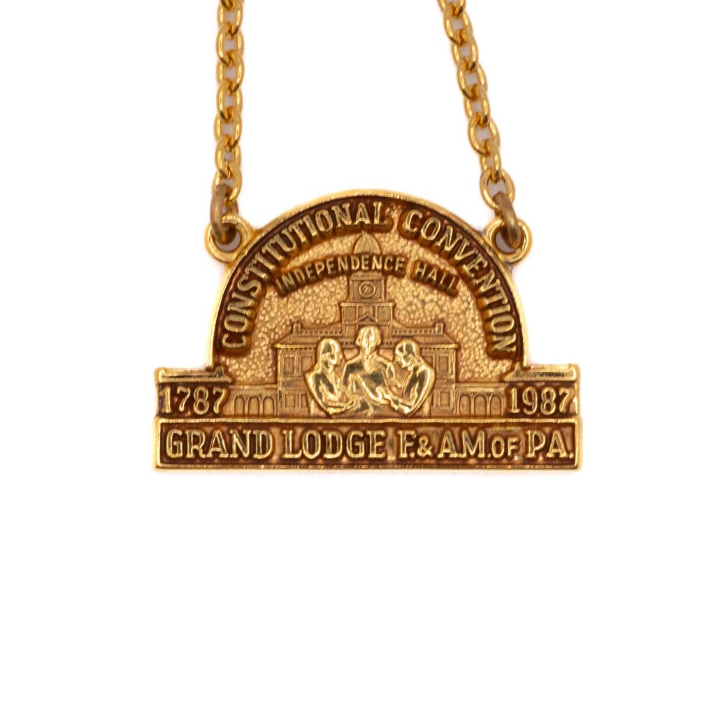 Gold tie chain with a pendant featuring text and image of men in front of Independence Hall on a white background
