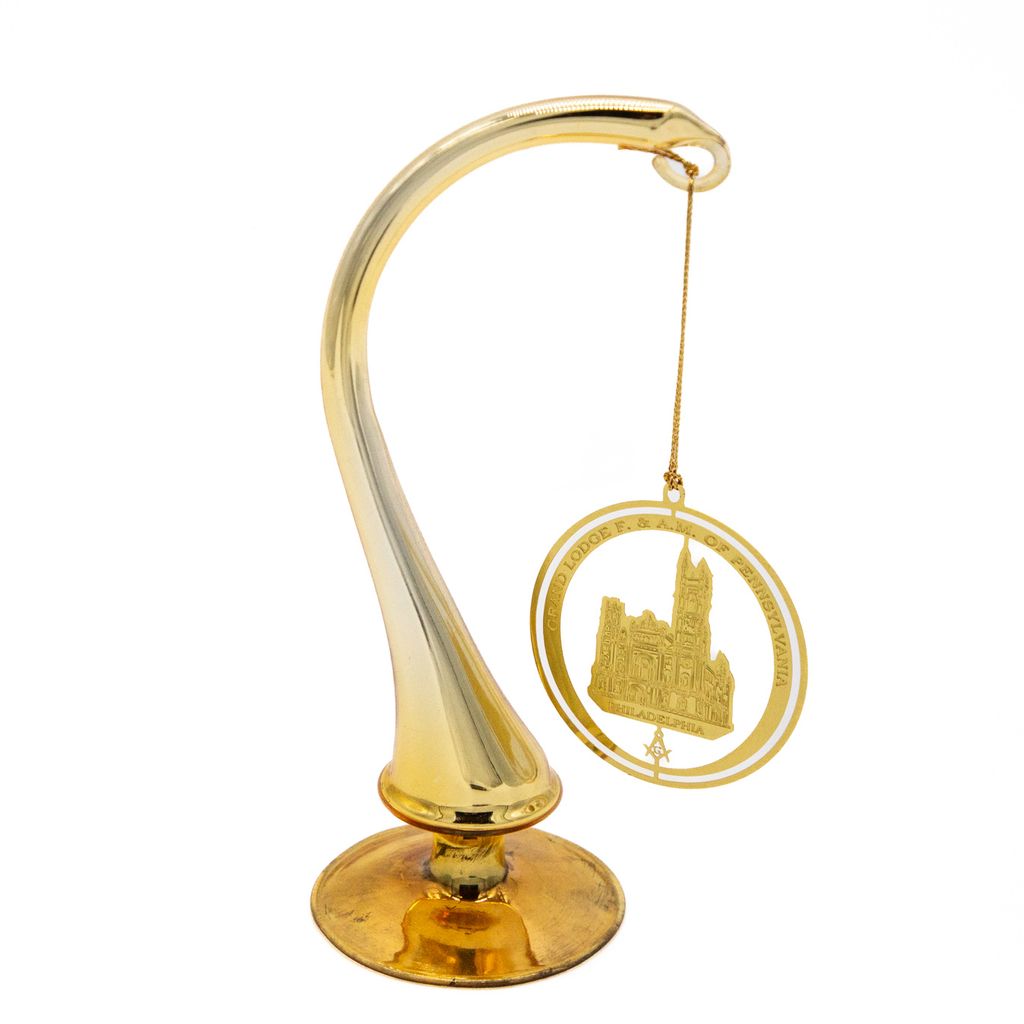 Gold decorative ornament with cutout of Masonic Temple with circle surrounding it hanging from a display hook. 