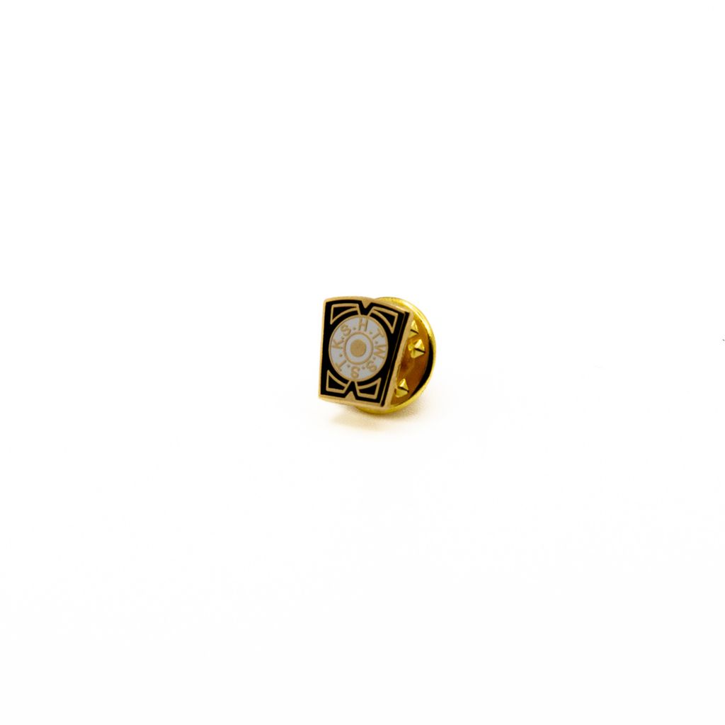Lapel pin featuring white circle in the center with gold letters and black border.