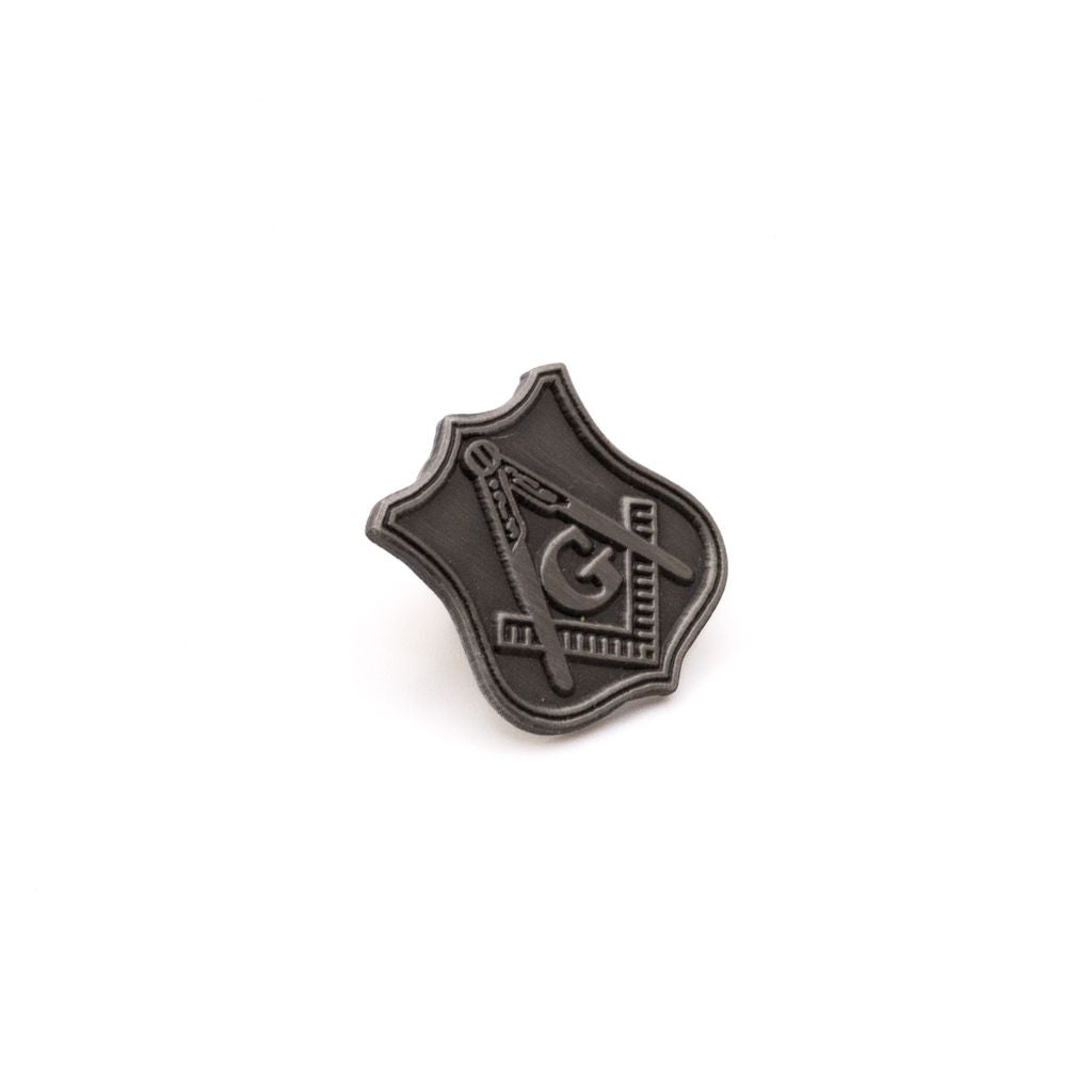 Square and Compass on a grey shield-shaped lapel pin with a white background