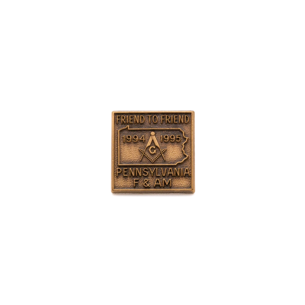 Bronze Masonic pin with text reading "Friend to Friend, 1994 1995, Pennsylvania F & AM," with outline of Pennsylvania and Square and Compass in center on a white background