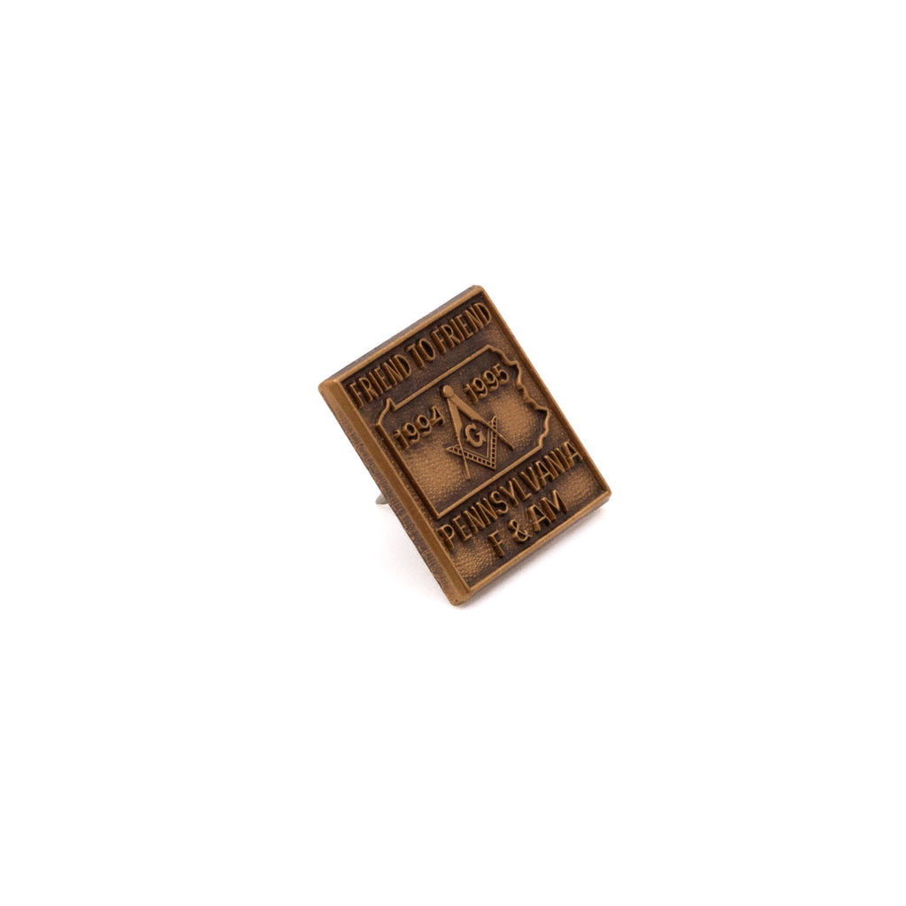 Bronze-colored metal pin with text and Pennsylvania state design on a white background